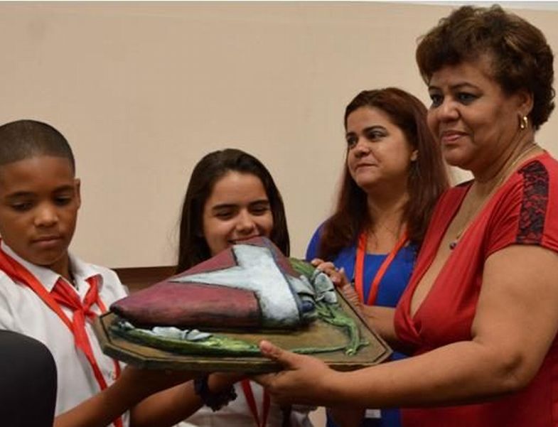 Olga Lidia Tapia recibe de manos de los pioneros un reconocimiento para Raúl Castro, una bandera cubana. (Foto: ACN)